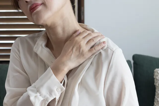 肩の痛みを感じ、肩を押さえる女性。四十肩・五十肩では痛みの強さに合わせて動きを調整する
